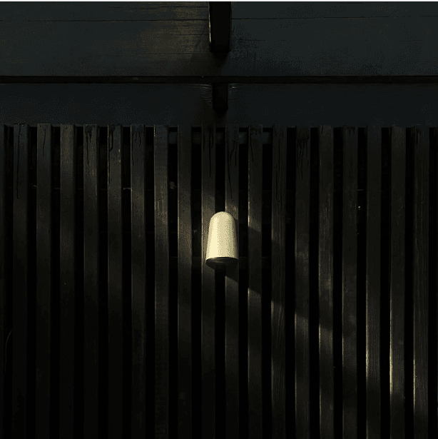 Brass wall sconce glowing against a blackened wood-slat fence at the Merz House garden